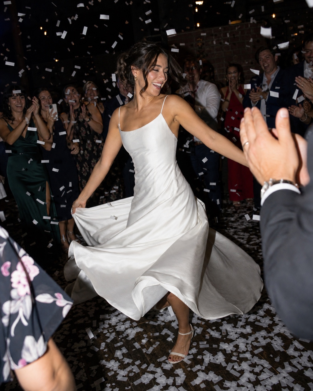 Bride dancing through falling confetti as cheering guests look on